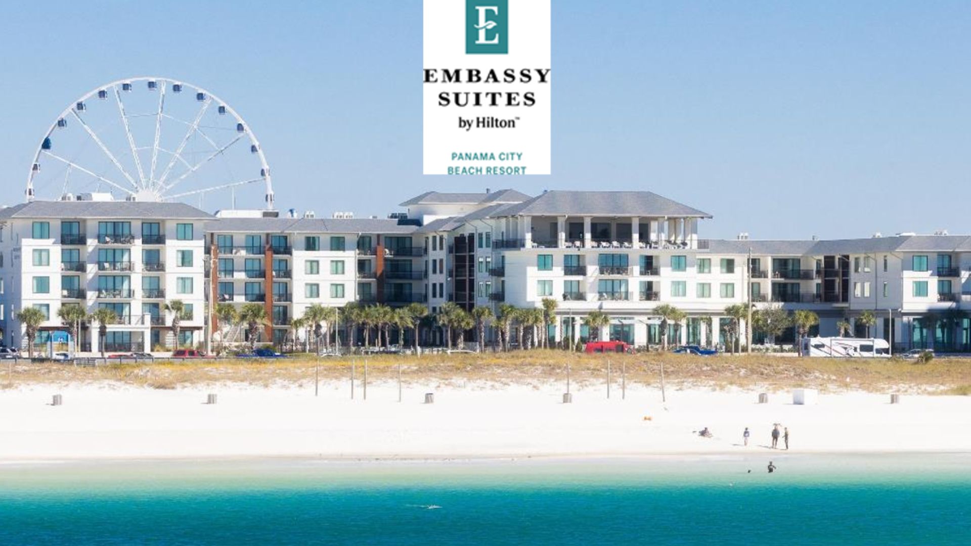 Beachfront Embassy Suites by Hilton Panama City Beach Resort with a large Ferris wheel in the background on a sunny day.